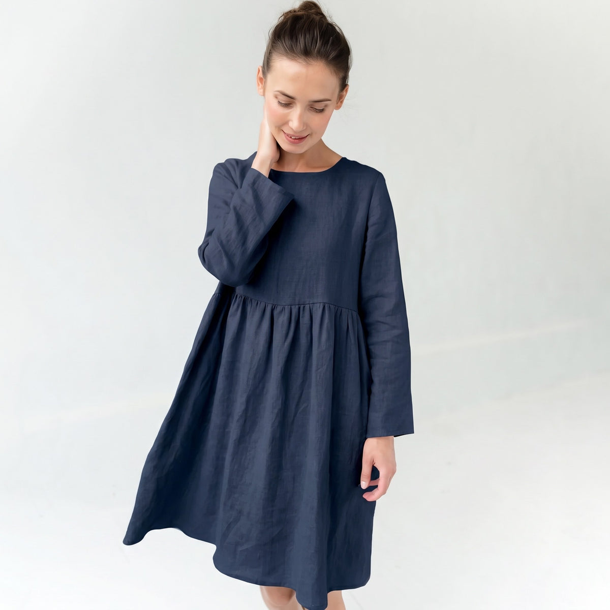 A woman wearing a navy blue long-sleeve linen dress with a gathered waist, standing against a light gray studio background.