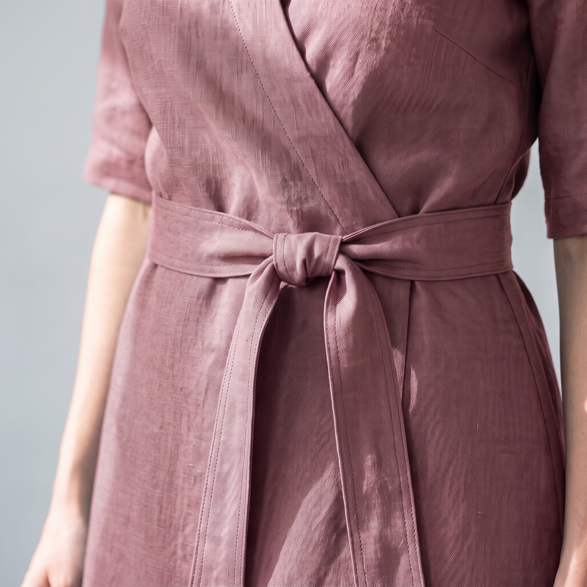 A close-up of a person wearing a dusty rose wrap dress with a matching waist tie, showing the textured fabric and waist details.
