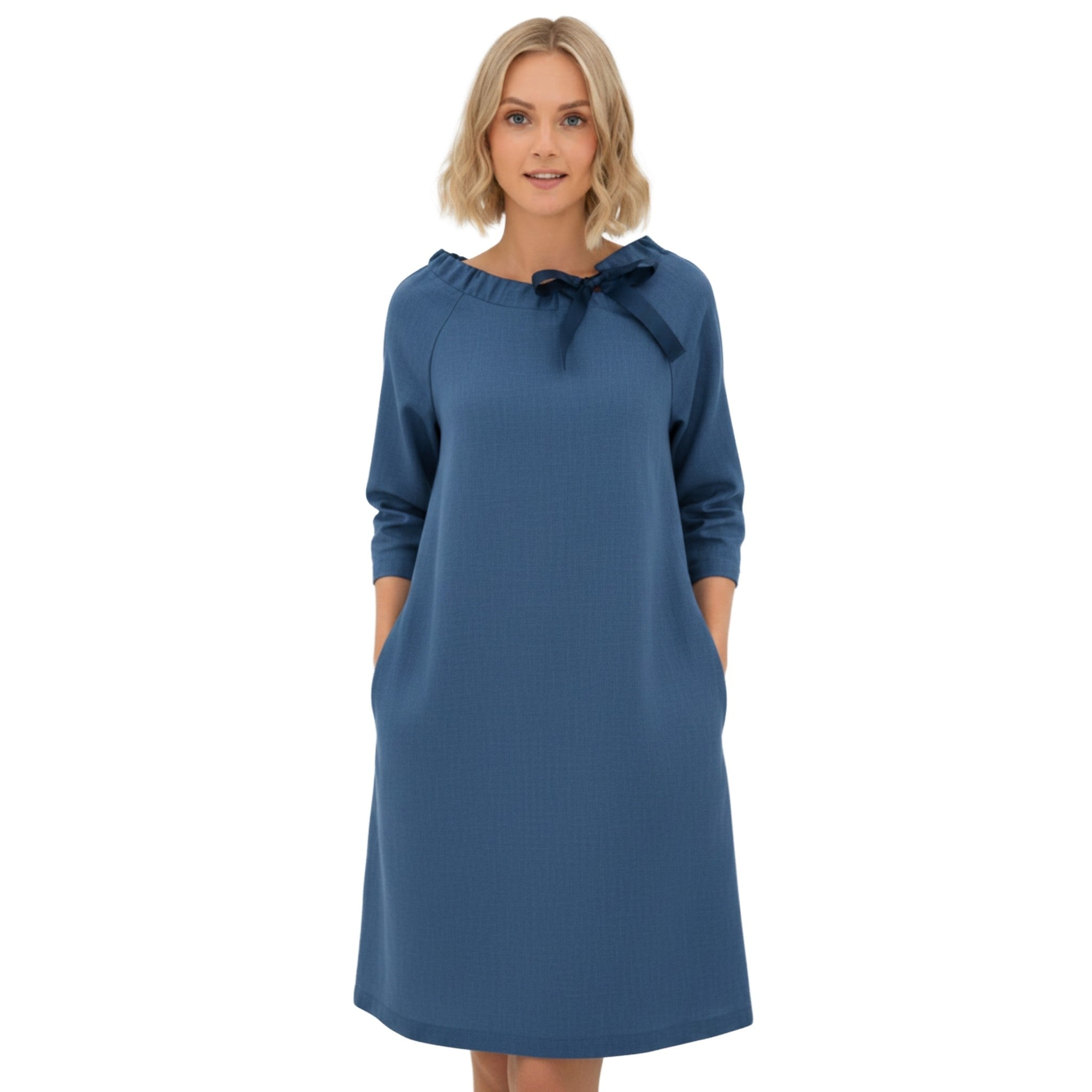 A woman modeling a state blue long-sleeve dress with a navy blue bow detail at the neckline, set against a plain white background.