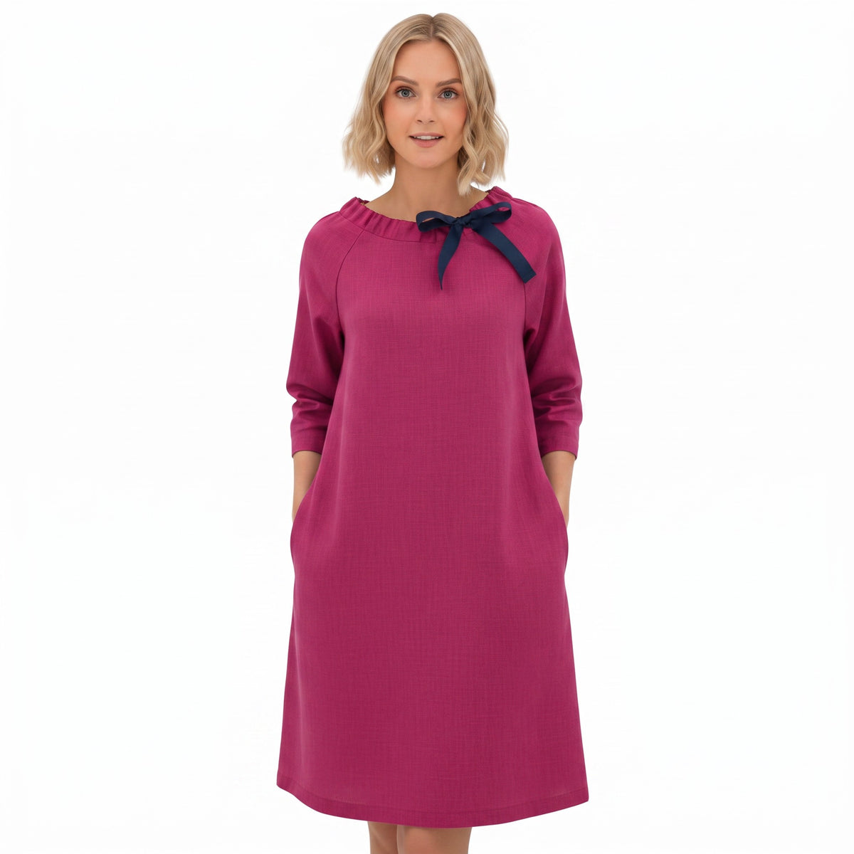 A woman modeling a magenta long-sleeve dress with a navy blue bow detail at the neckline, set against a plain white background.
