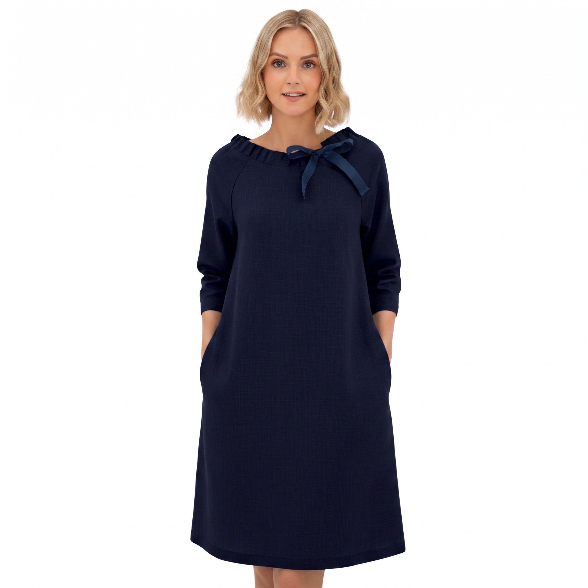 A woman modeling a dark navy blue long-sleeve dress with a navy blue bow detail at the neckline, set against a plain white background.