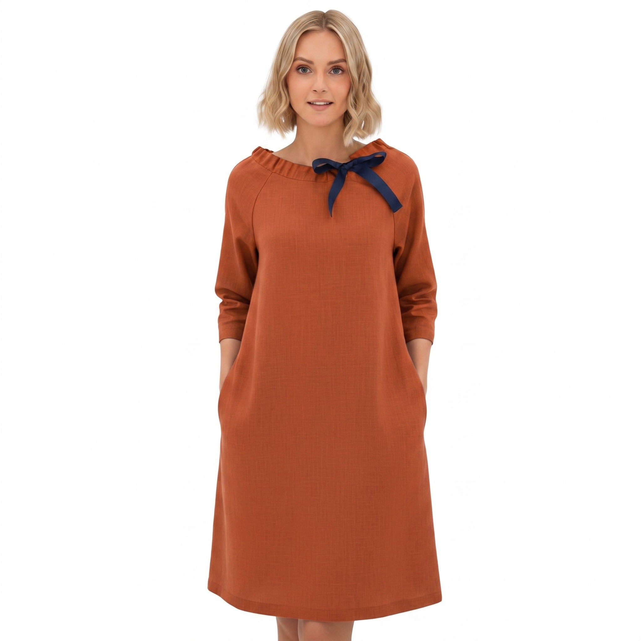 A woman modeling a rust-orange long-sleeve dress with a navy blue bow detail at the neckline, set against a plain white background.