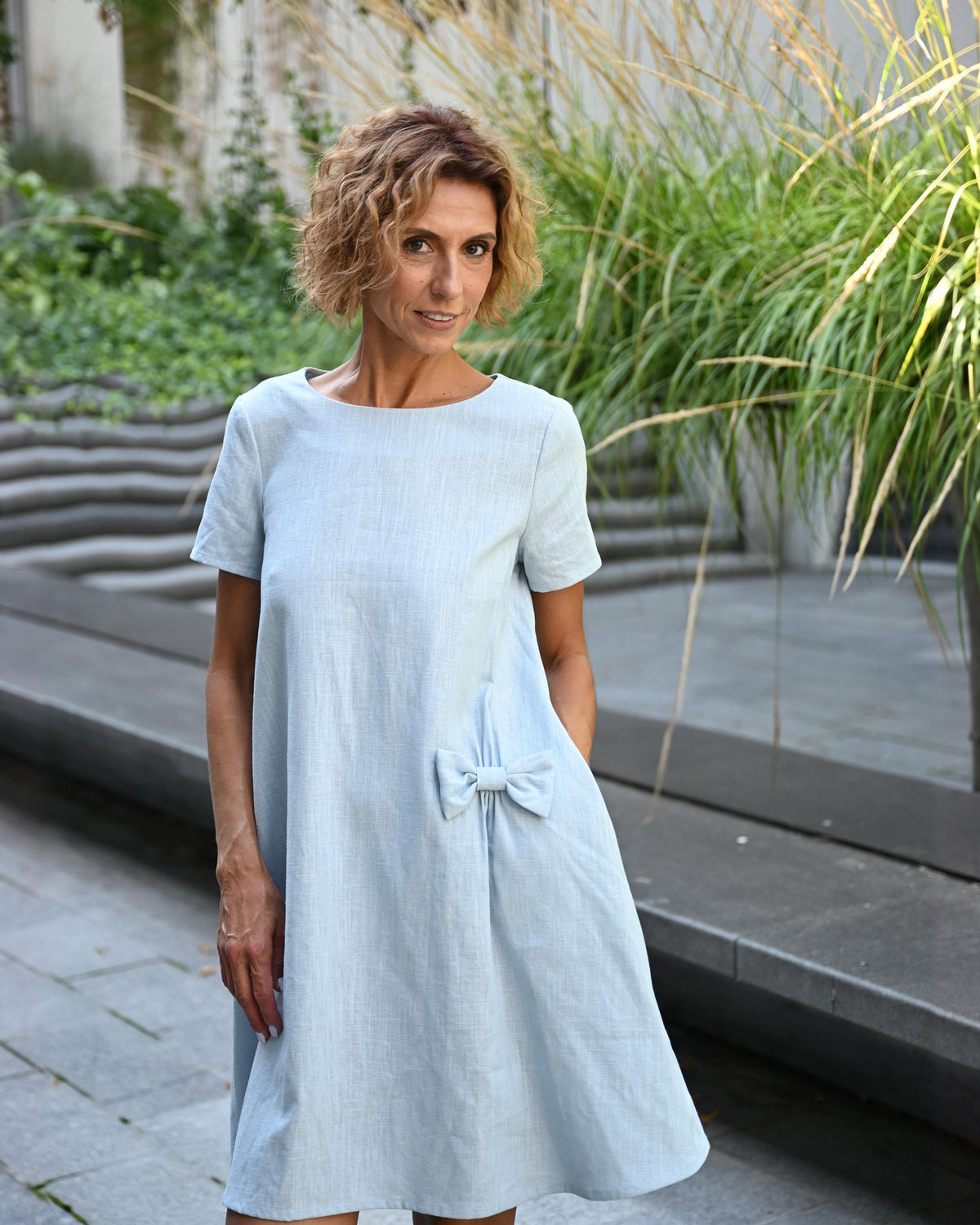 LeMuse SUMMER KISS linen dress in light blue – outdoor front view, hands in pockets #Color_Light blue