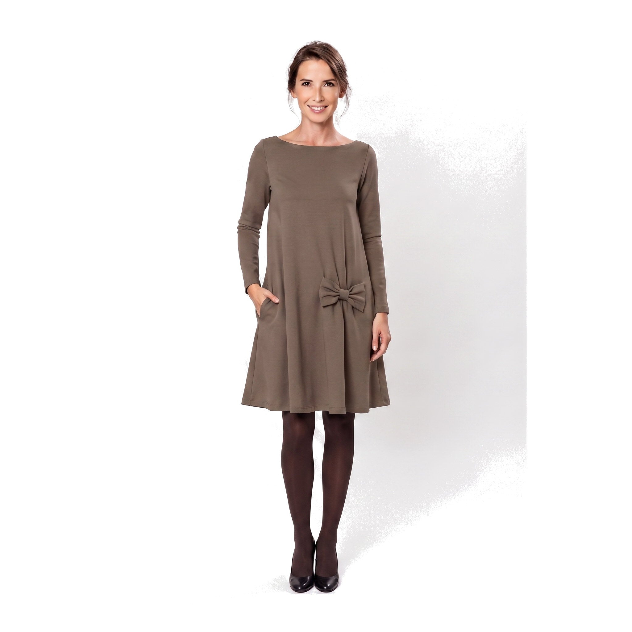 A woman modeling a brown long-sleeve A-line dress with a boat neckline, side pockets, and a bow detail at the waist.
