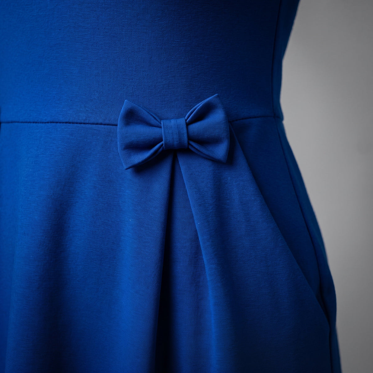 A royal blue long-sleeve knee-length dress with a structured waist and bow details.