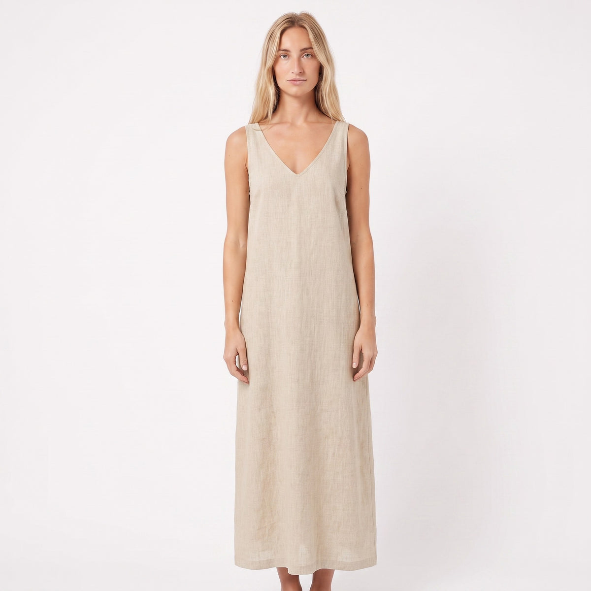A woman modeling a sleeveless, V-neck maxi dress in a light beige linen-like fabric against a plain white studio background.