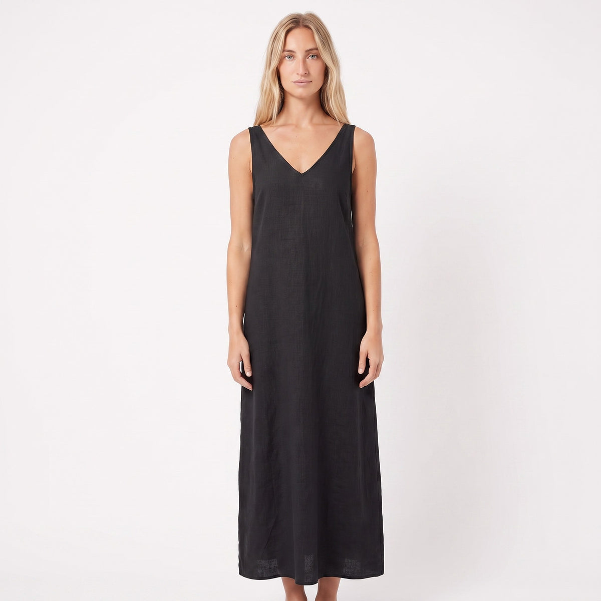 A woman modeling a sleeveless black midi dress with a V-neckline, standing against a plain white studio background.