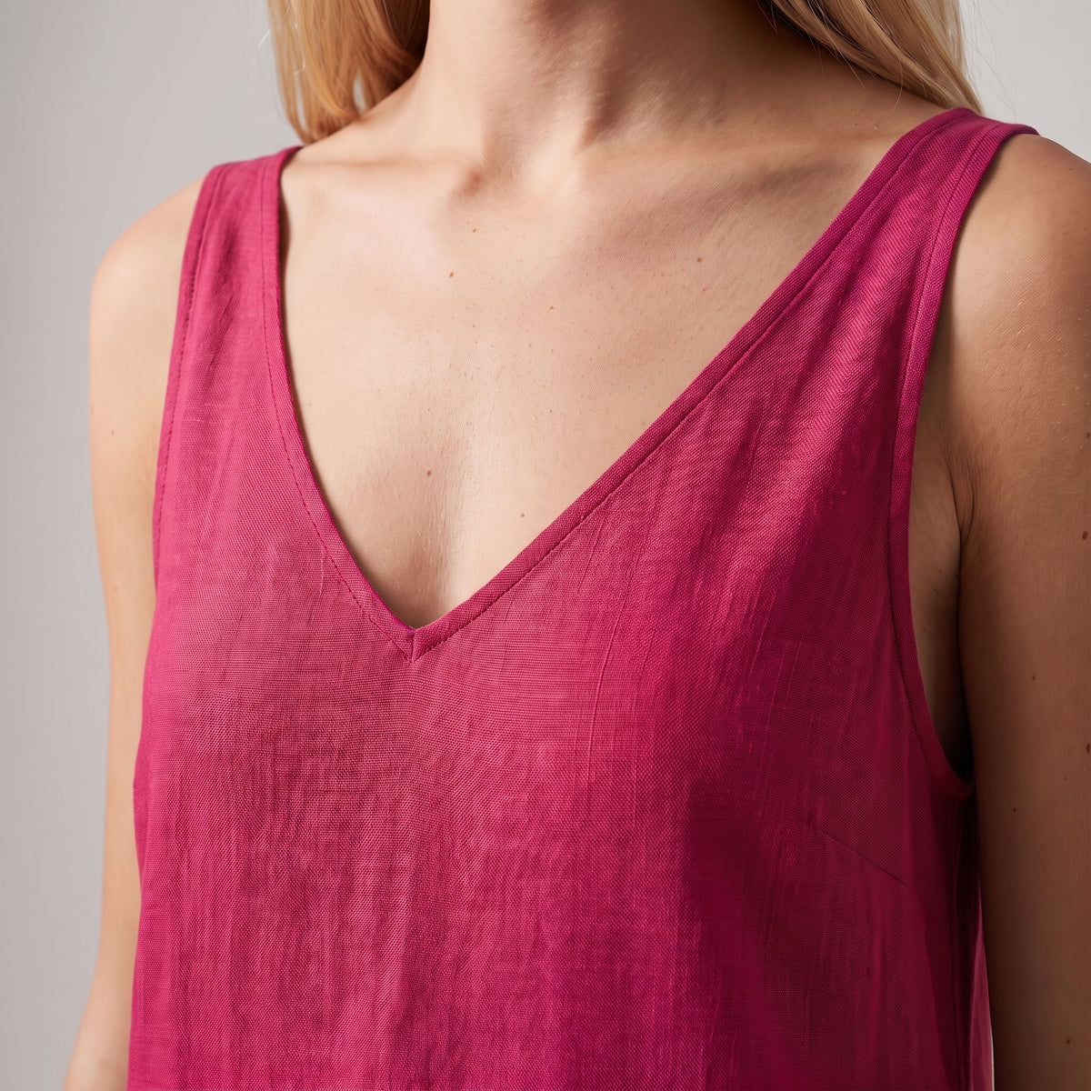 A close-up of a woman wearing a sleeveless V-neck top in a rich magenta pink color, showing the texture of the fabric.