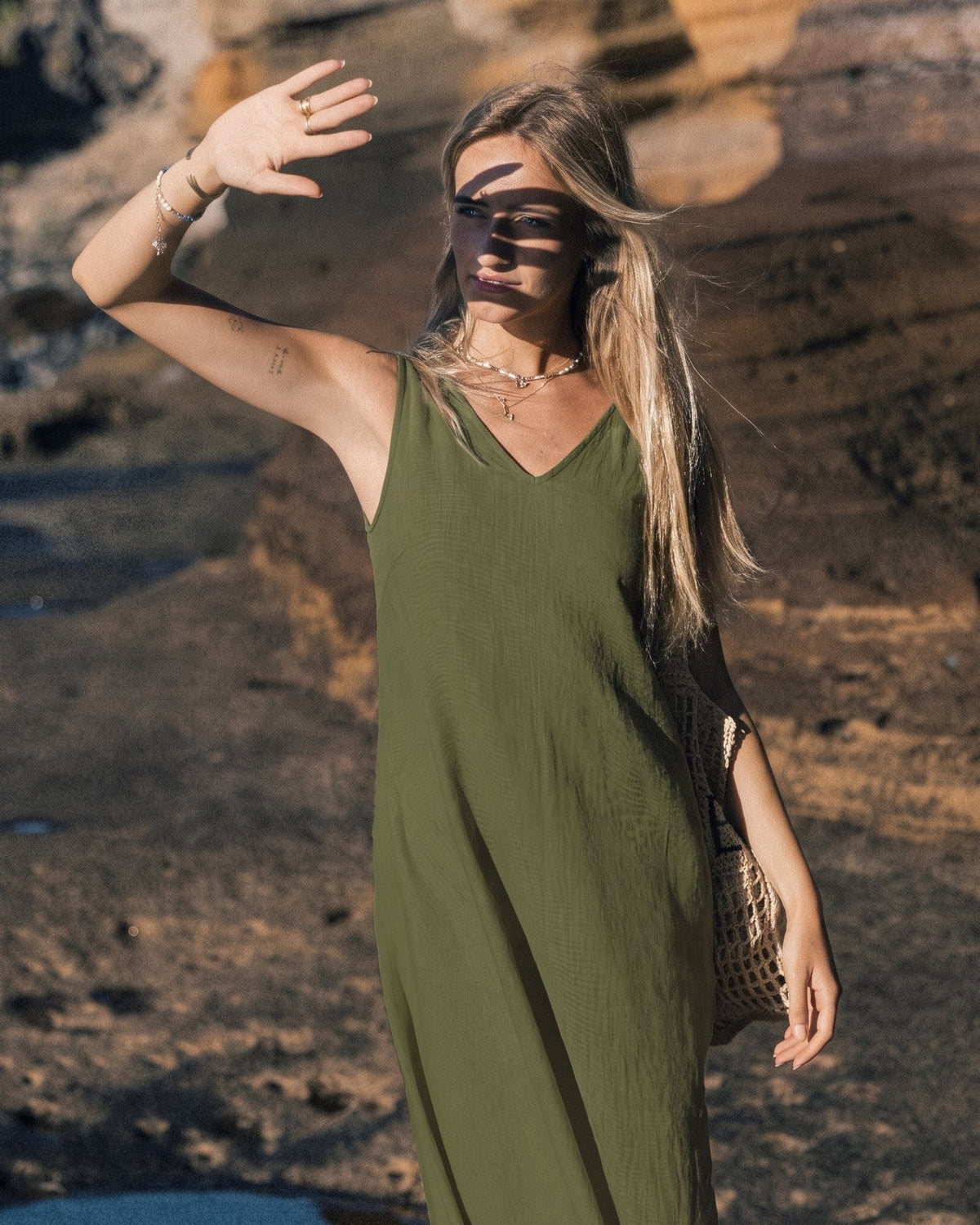 LeMuse SUNSET linen dress in olive green – model in motion with arm raised on the cliffs #Color_Olive green