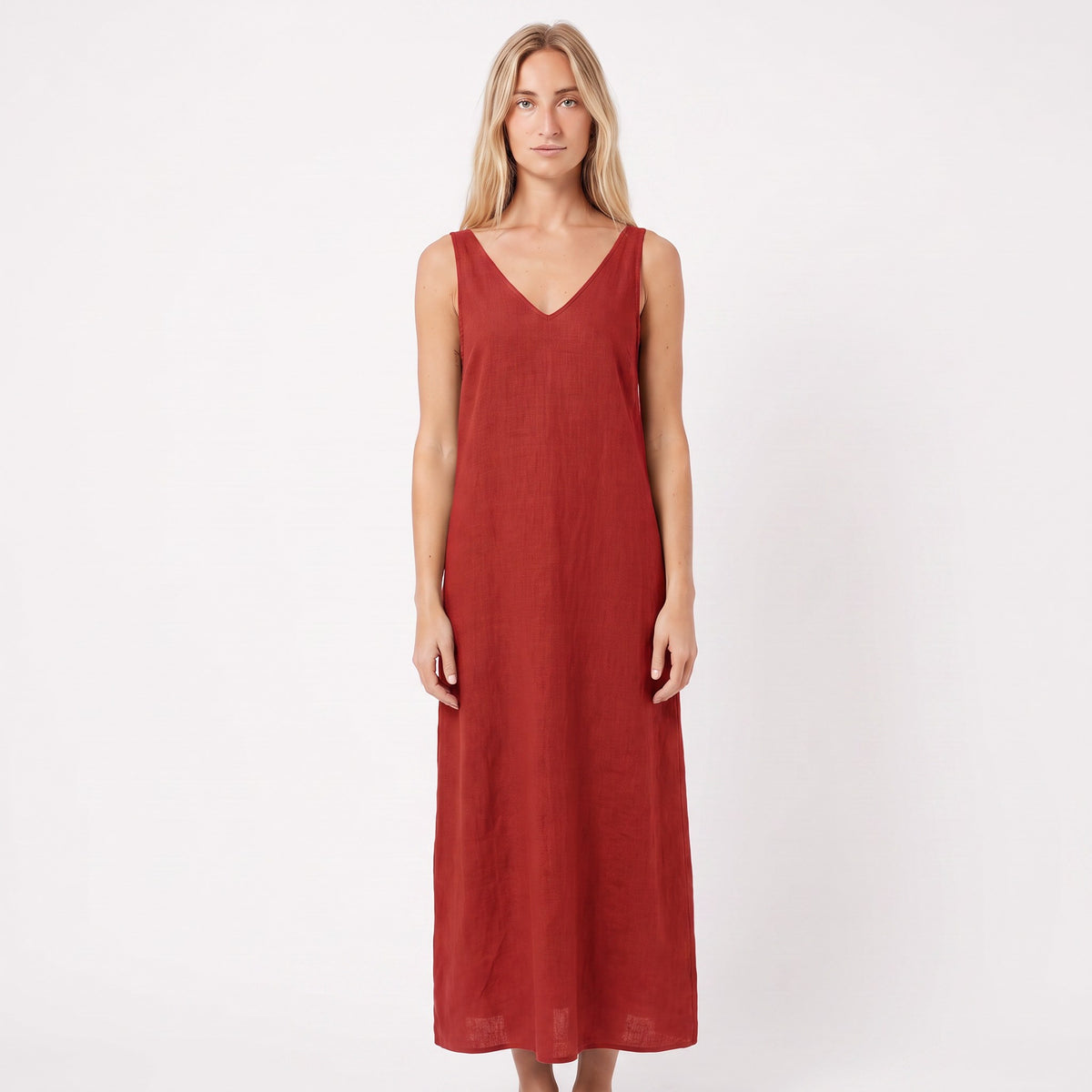 A woman modeling a sleeveless, V-neck maxi dress in a rust red color, standing against a plain white studio background.
