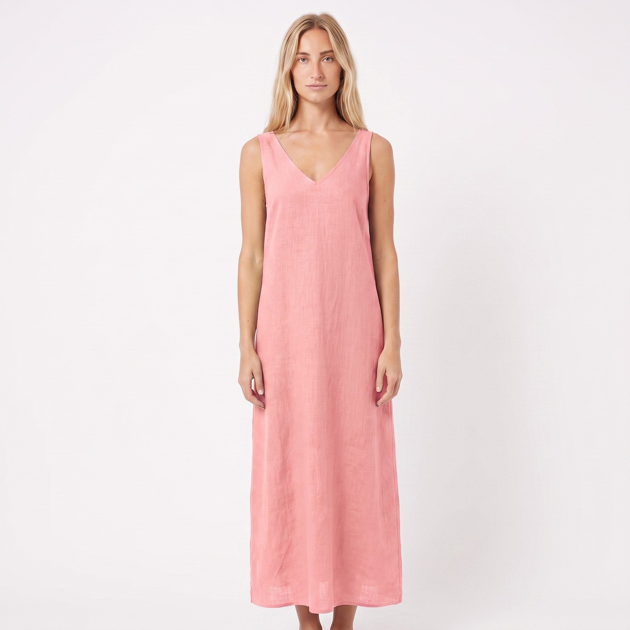 A woman modeling a sleeveless, V-neck maxi dress in a soft dusty pink color, standing against a plain white studio background.