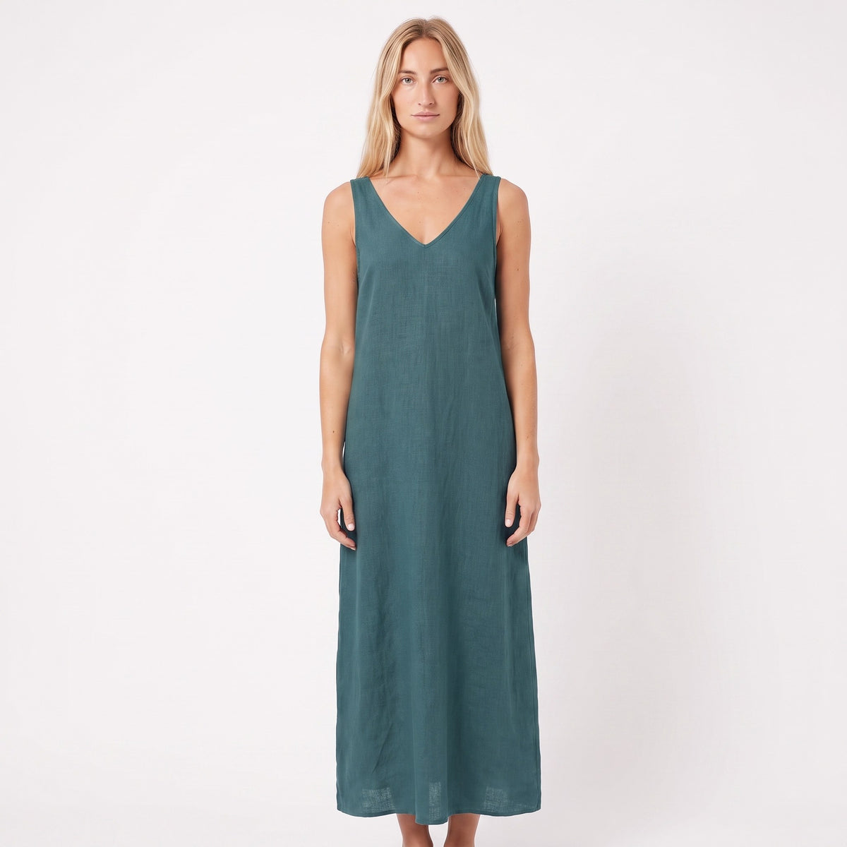 A woman modeling a sleeveless, V-neck maxi dress in a muted teal green color, standing against a plain white studio background.