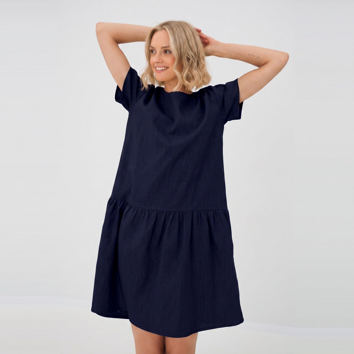A woman modeling a short-sleeve navy blue tiered dress against a plain white studio background.