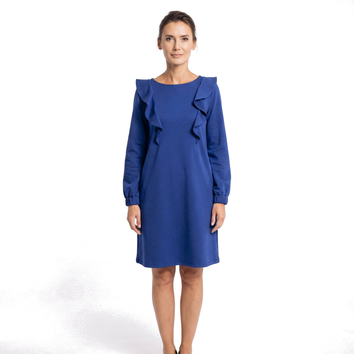 A woman modeling a royal blue long-sleeve dress with ruffle detailing on the shoulders, photographed against a clean white studio background.
