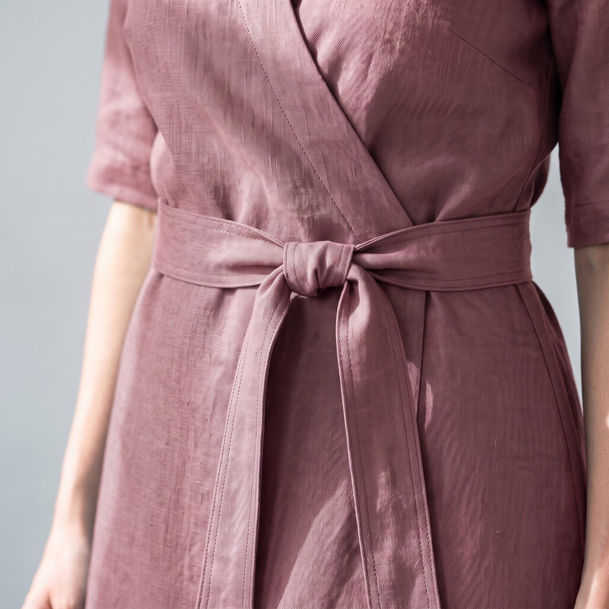 A close-up of a person wearing a dusty rose wrap dress with a matching waist tie, showing the textured fabric and waist details.