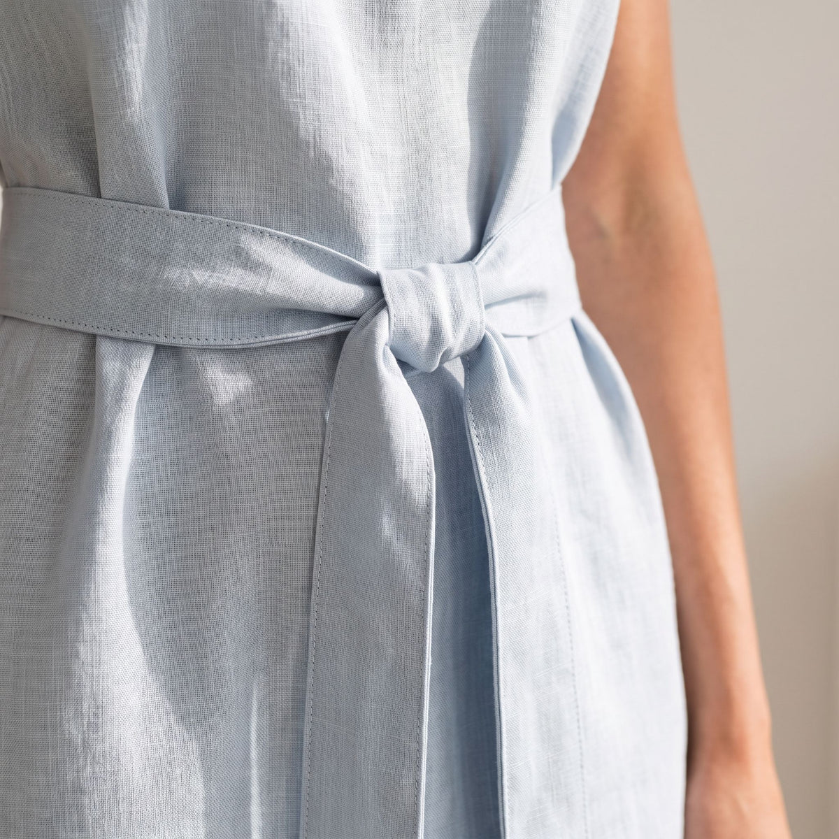 Close-up of a light blue linen dress with a matching tie belt, worn by a model.