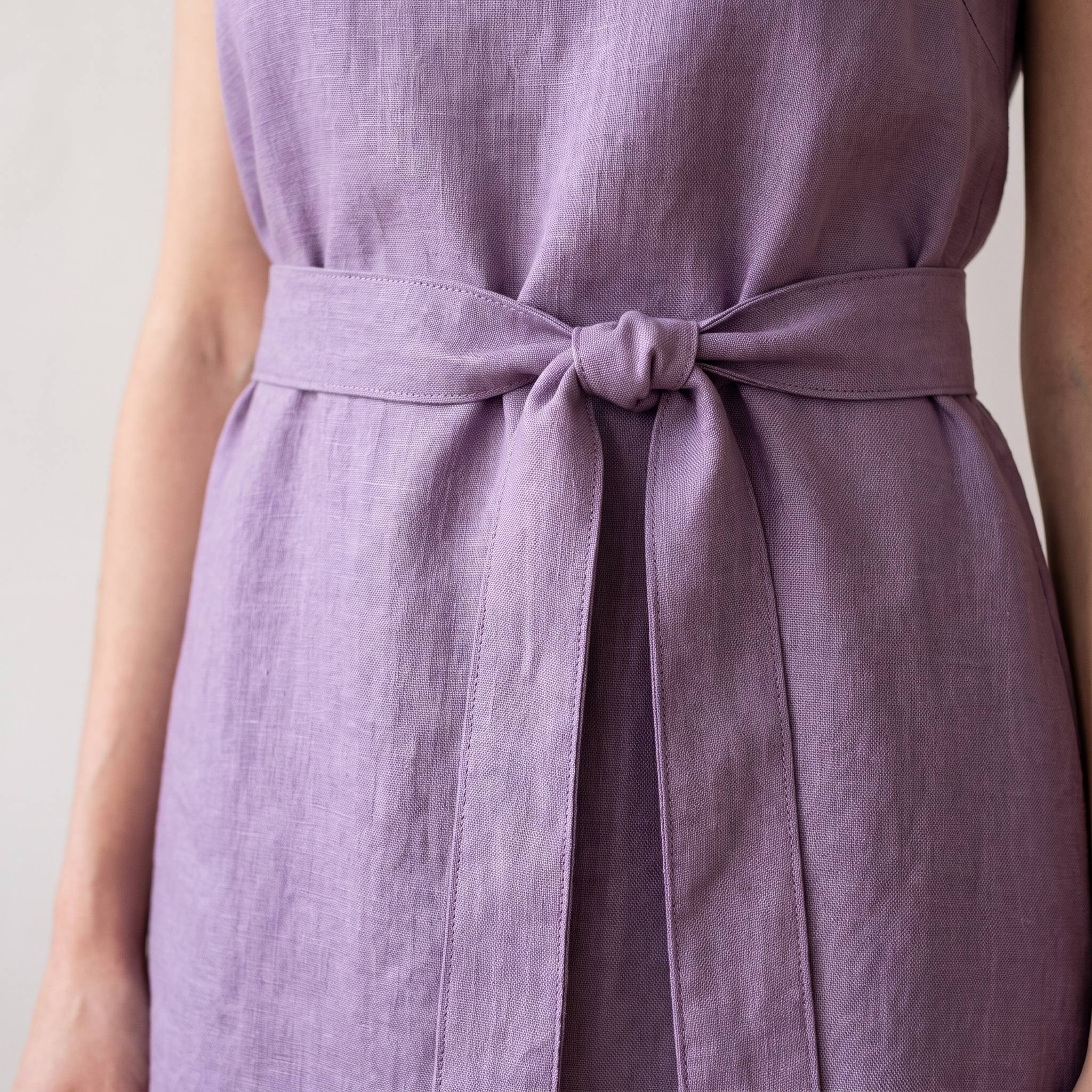 Close-up of a person wearing a sleeveless lavender-purple dress with a matching fabric tie belt at the waist, shown against a plain light background.
