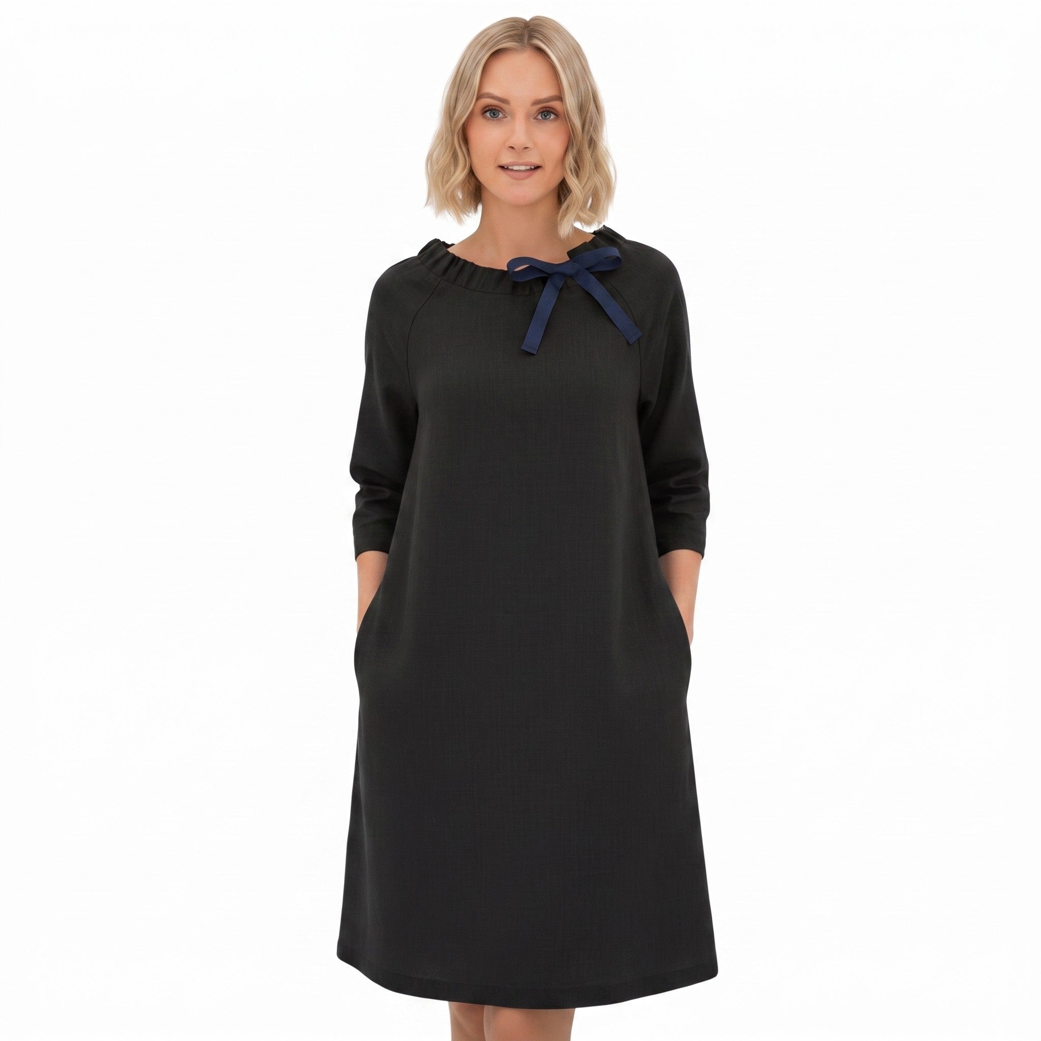 A woman modeling a black long-sleeve dress with a navy blue bow detail at the neckline, set against a plain white background.