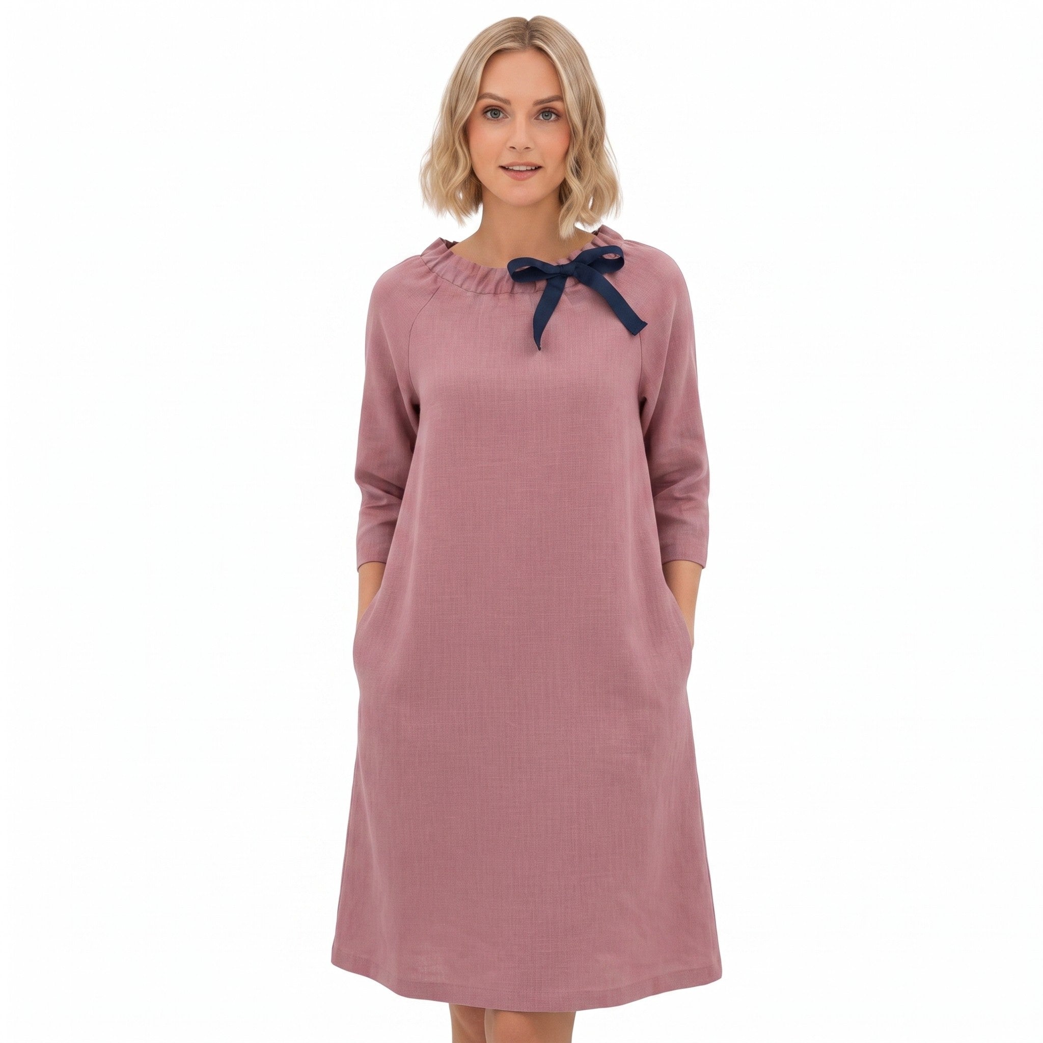A woman modeling a dusty rose long-sleeve dress with a navy blue bow detail at the neckline, set against a plain white background.