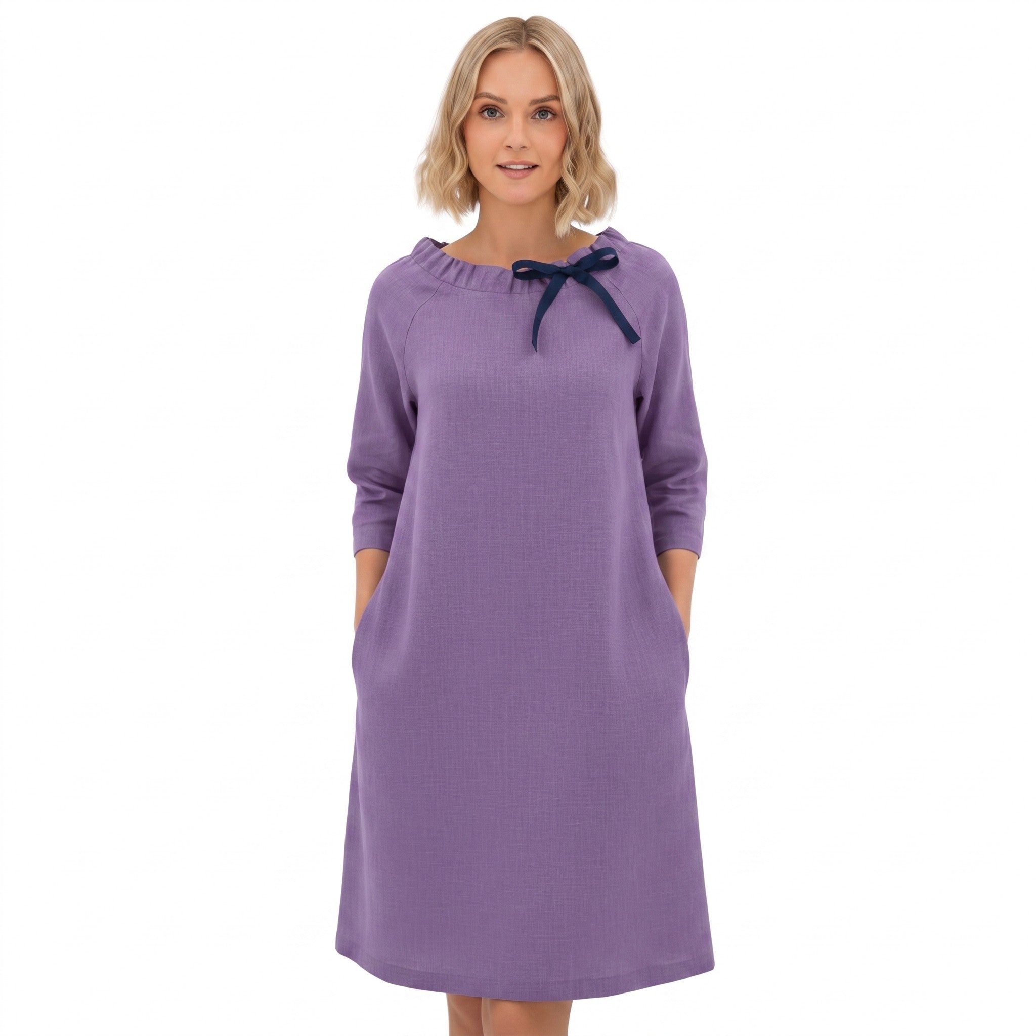 A woman modeling a lavender-purple long-sleeve dress with a navy blue bow detail at the neckline, set against a plain white background.
