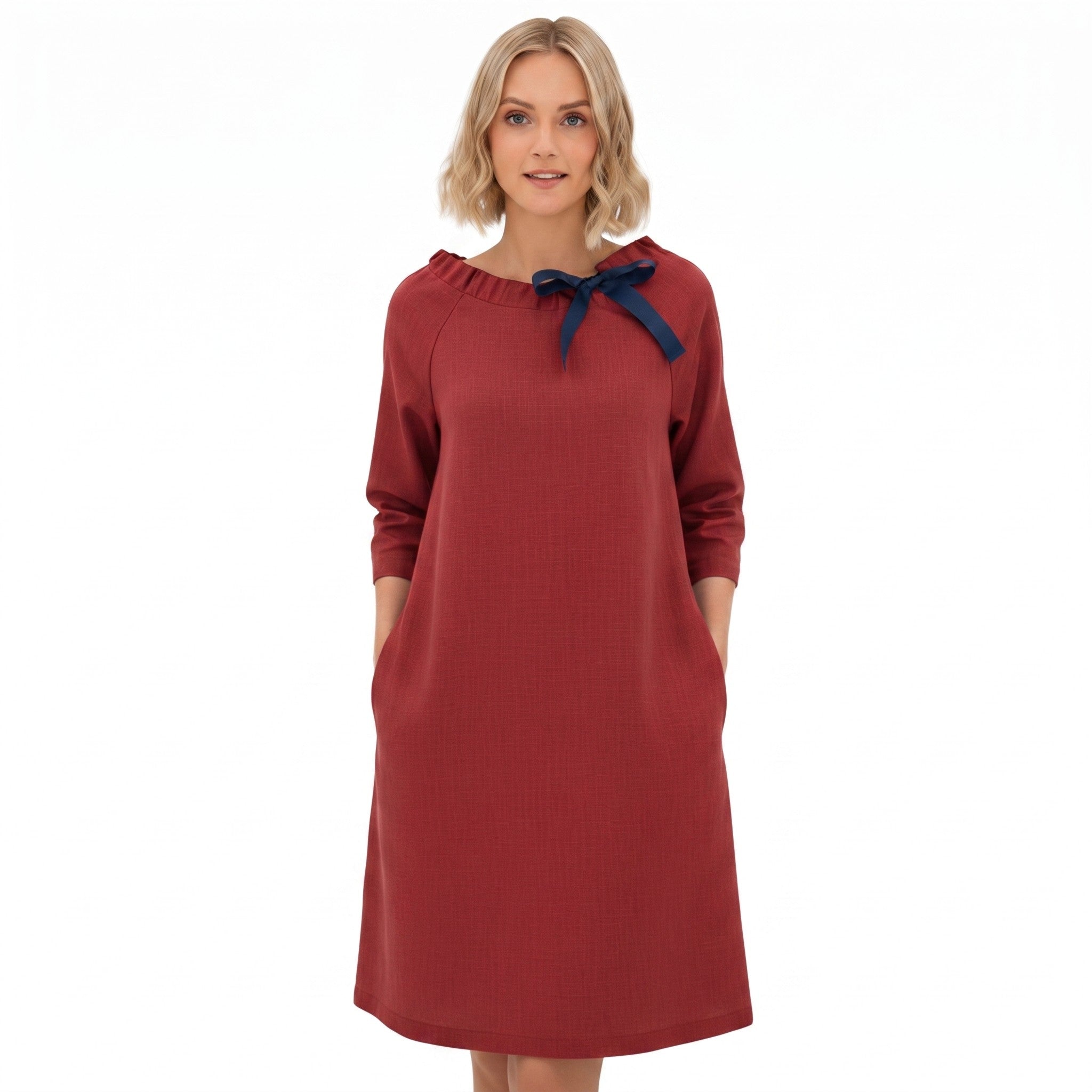 A woman modeling a rust-red long-sleeve dress with a navy blue bow detail at the neckline, set against a plain white background.
