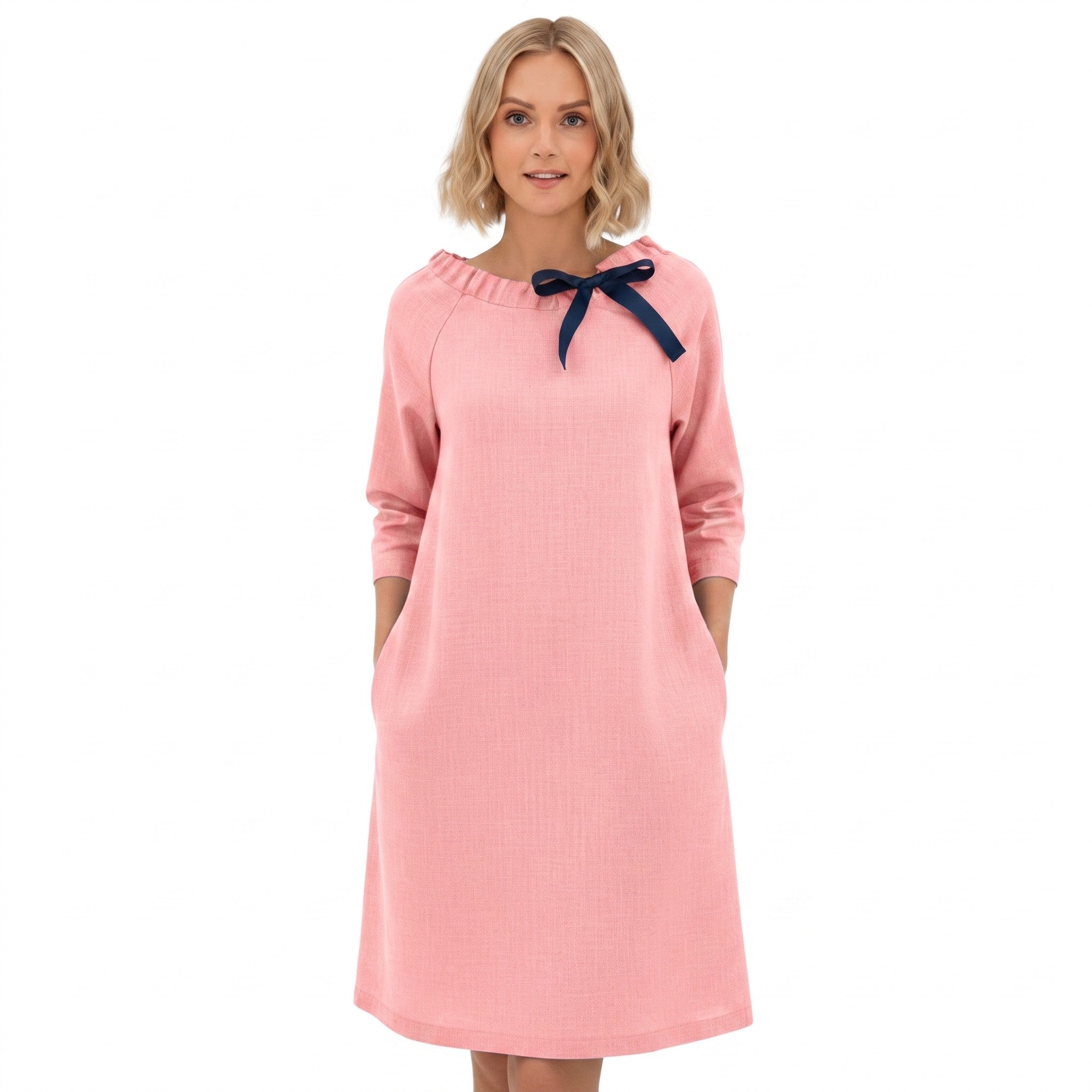 A woman modeling a light pink long-sleeve dress with a navy blue bow detail at the neckline, set against a plain white background.