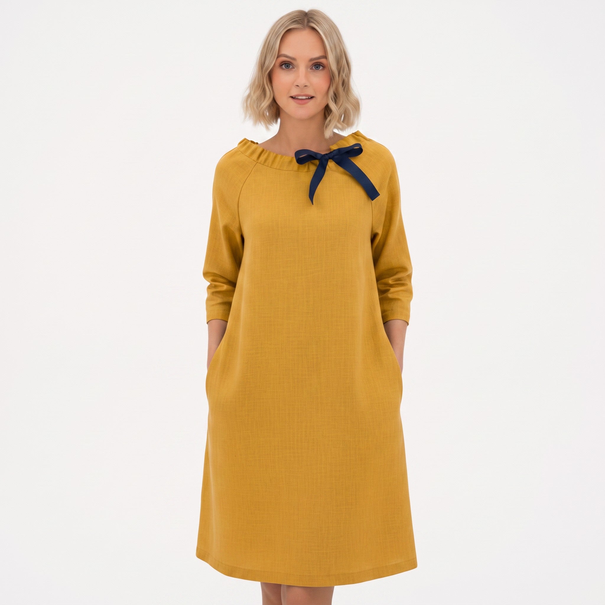 A woman modeling a yellow long-sleeve dress with a navy blue bow detail at the neckline, set against a plain white background.