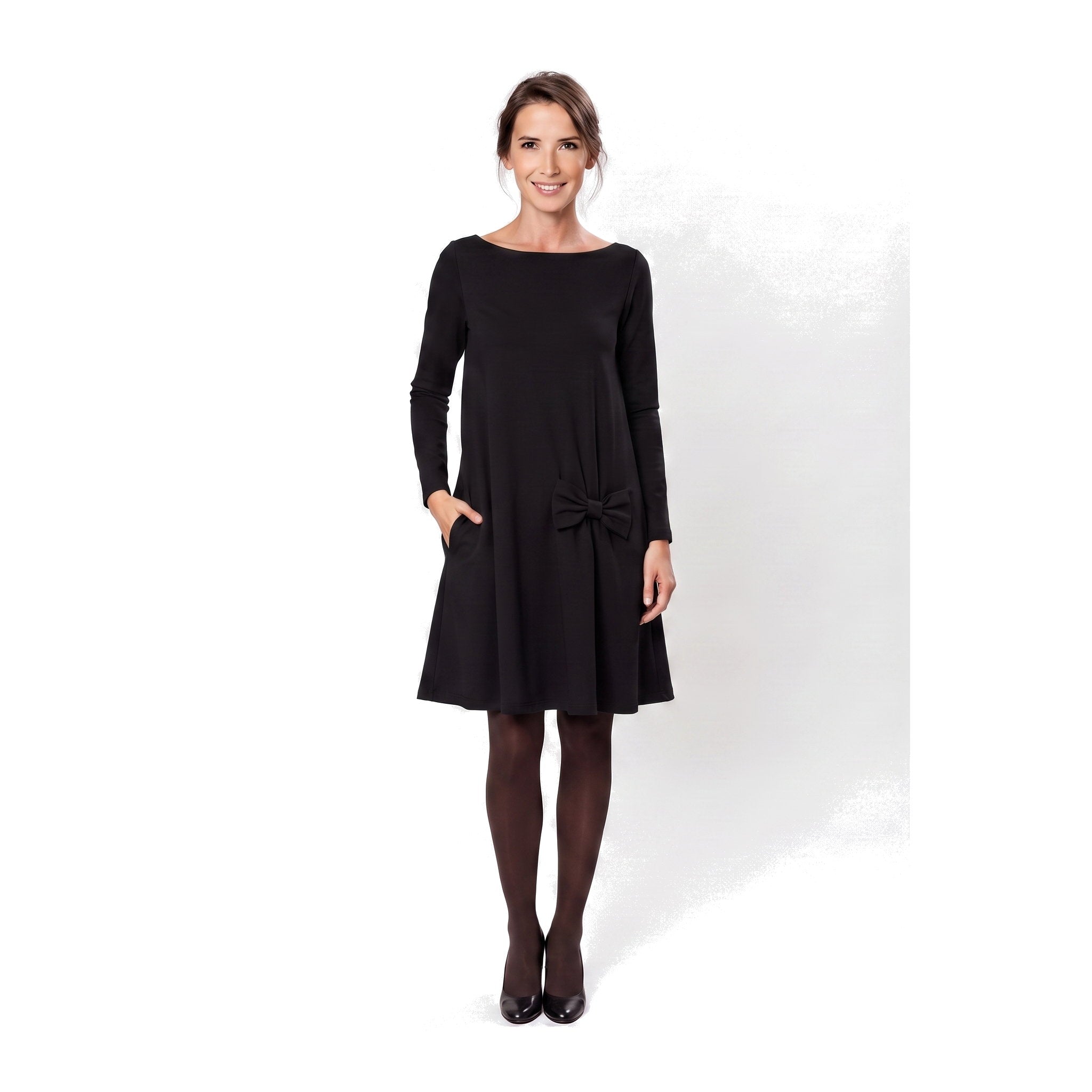 A woman modeling a black long-sleeve A-line dress with a boat neckline, side pockets, and a bow detail at the waist.