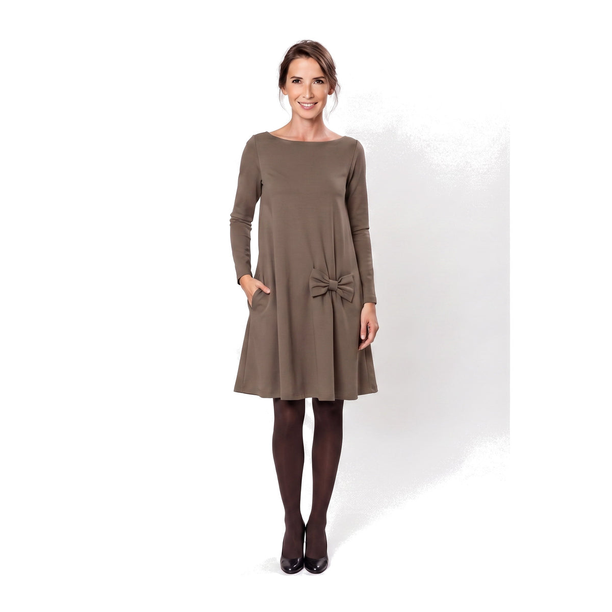 A woman modeling a brown long-sleeve A-line dress with a boat neckline, side pockets, and a bow detail at the waist.