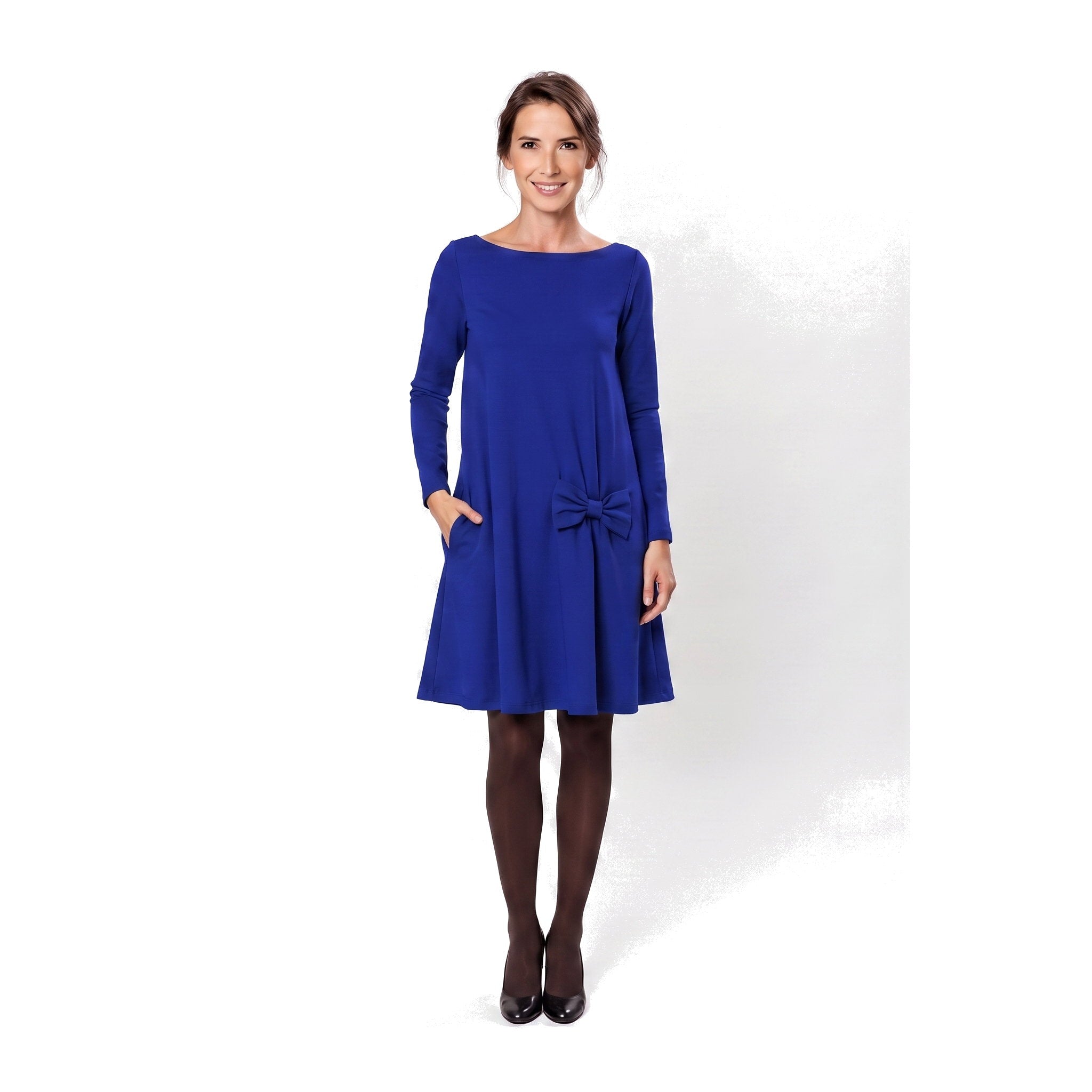 A woman modeling a royal blue long-sleeve A-line dress with a boat neckline, side pockets, and a bow detail at the waist.