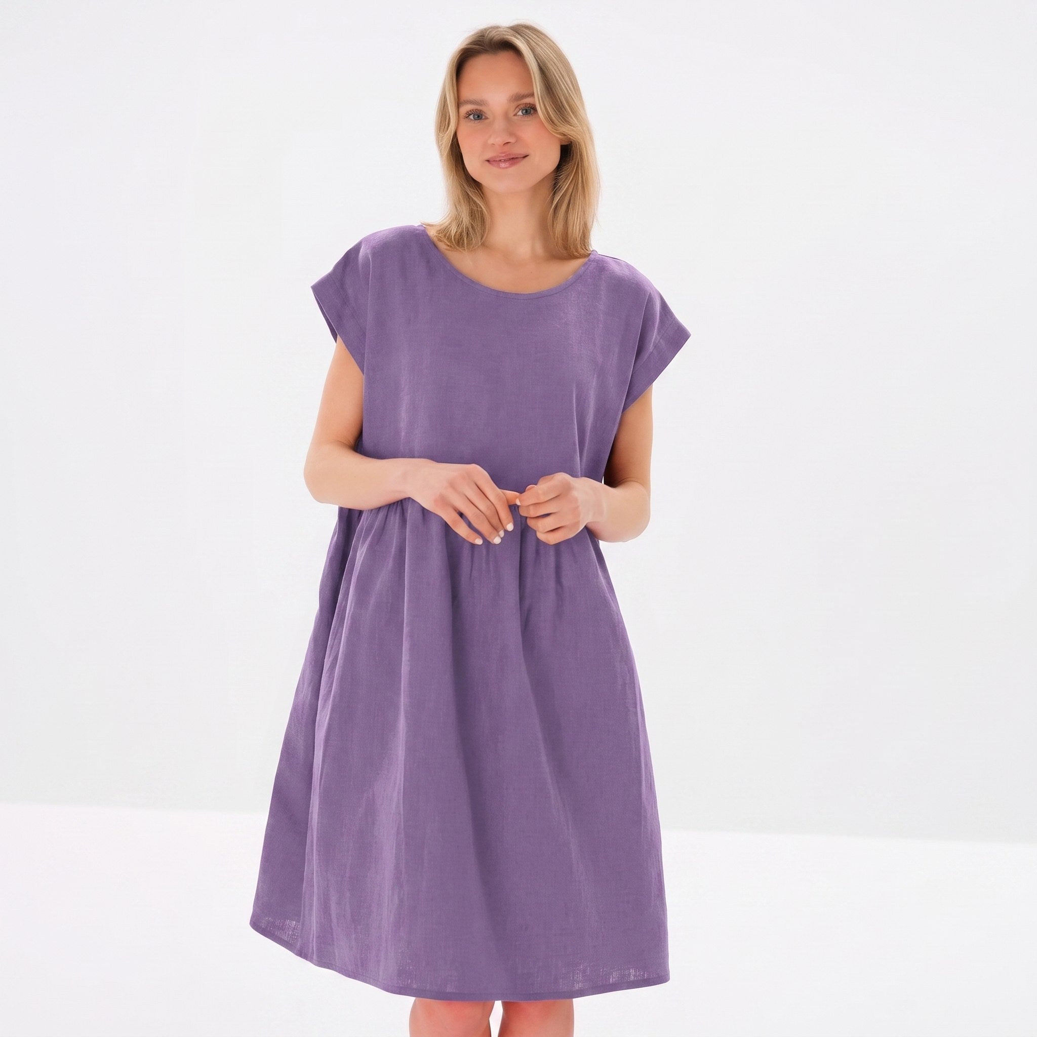 A woman modeling a loose, short-sleeved purple dress against a clean white studio background.
