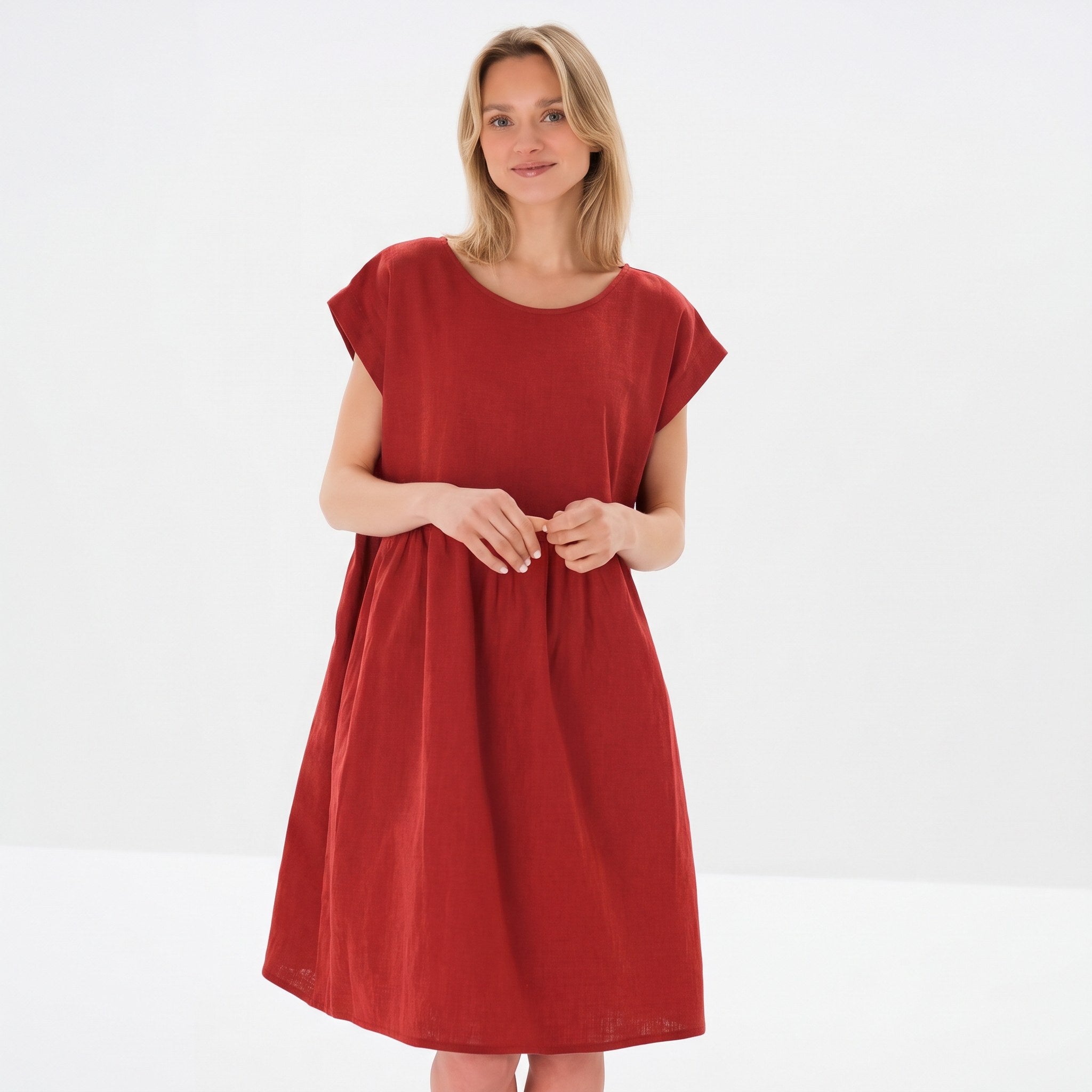 A woman modeling a loose-fitting, short-sleeved red dress against a clean white studio background.