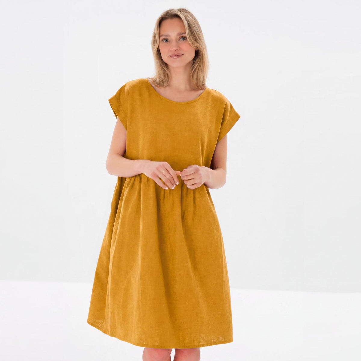 A woman modeling a loose, short-sleeved midi dress in a solid mustard yellow color, set against a clean white studio background.