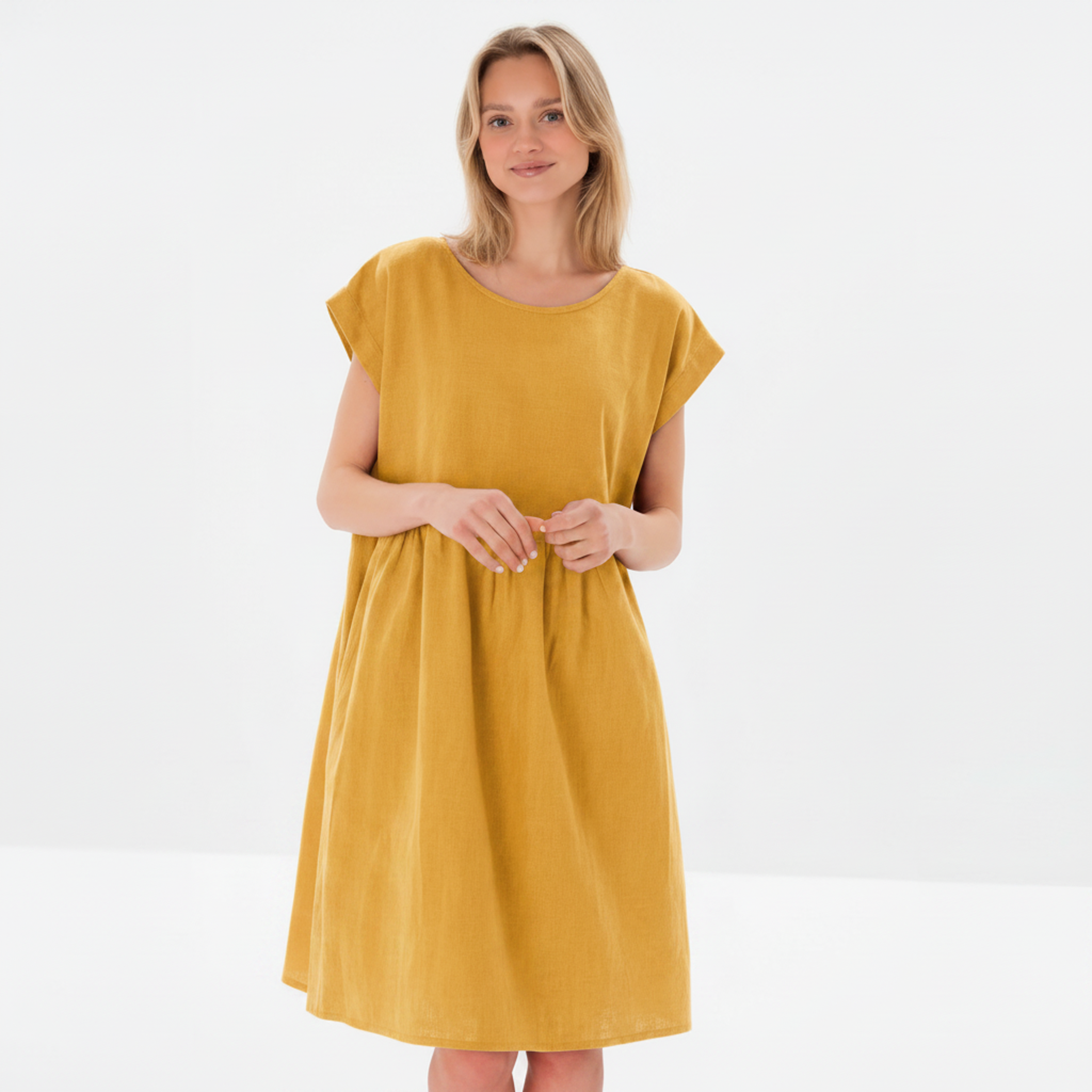 A woman modeling a mustard yellow linen dress with a relaxed, loose fit, short cap sleeves, and a round neckline against a clean white studio background.
