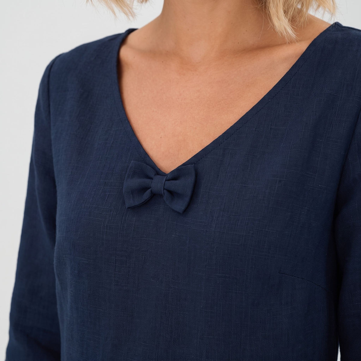 Close-up of a woman wearing a navy blue long-sleeve top with a V-neck and a small bow detail at the center of the chest.
