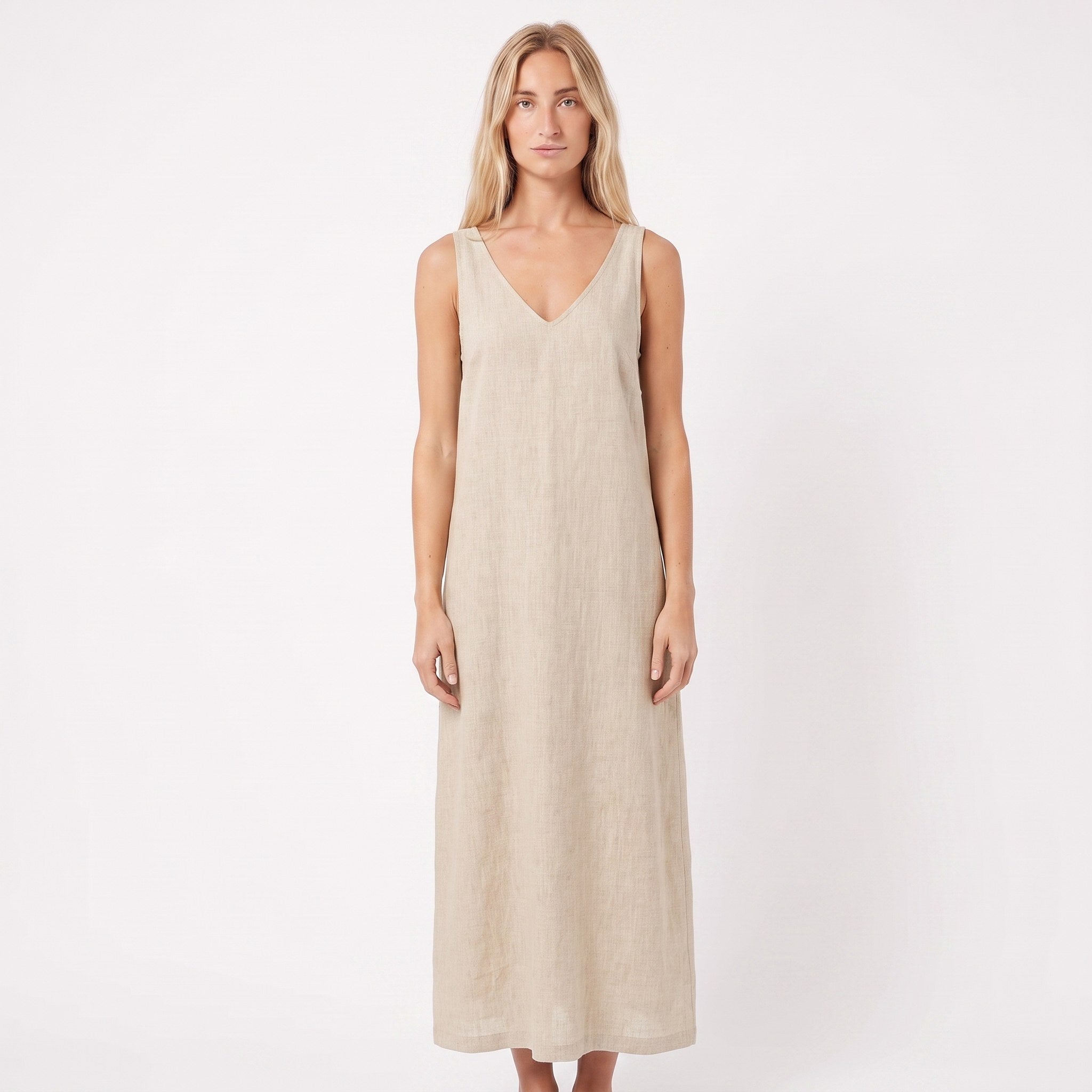 A woman modeling a sleeveless, V-neck maxi dress in a light beige linen-like fabric against a plain white studio background.