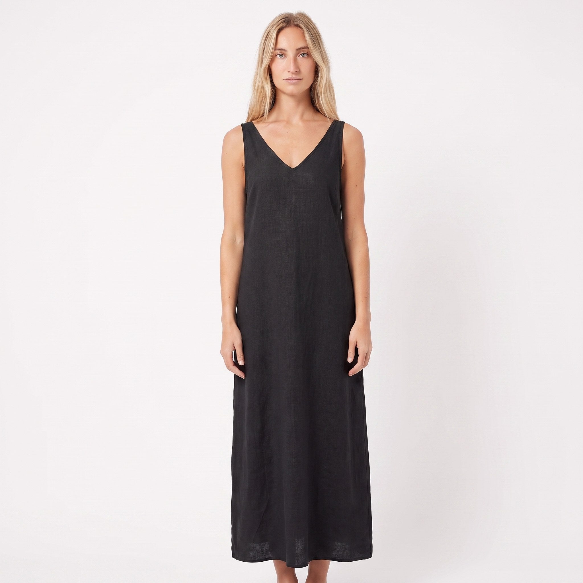 A woman modeling a sleeveless black midi dress with a V-neckline, standing against a plain white studio background.