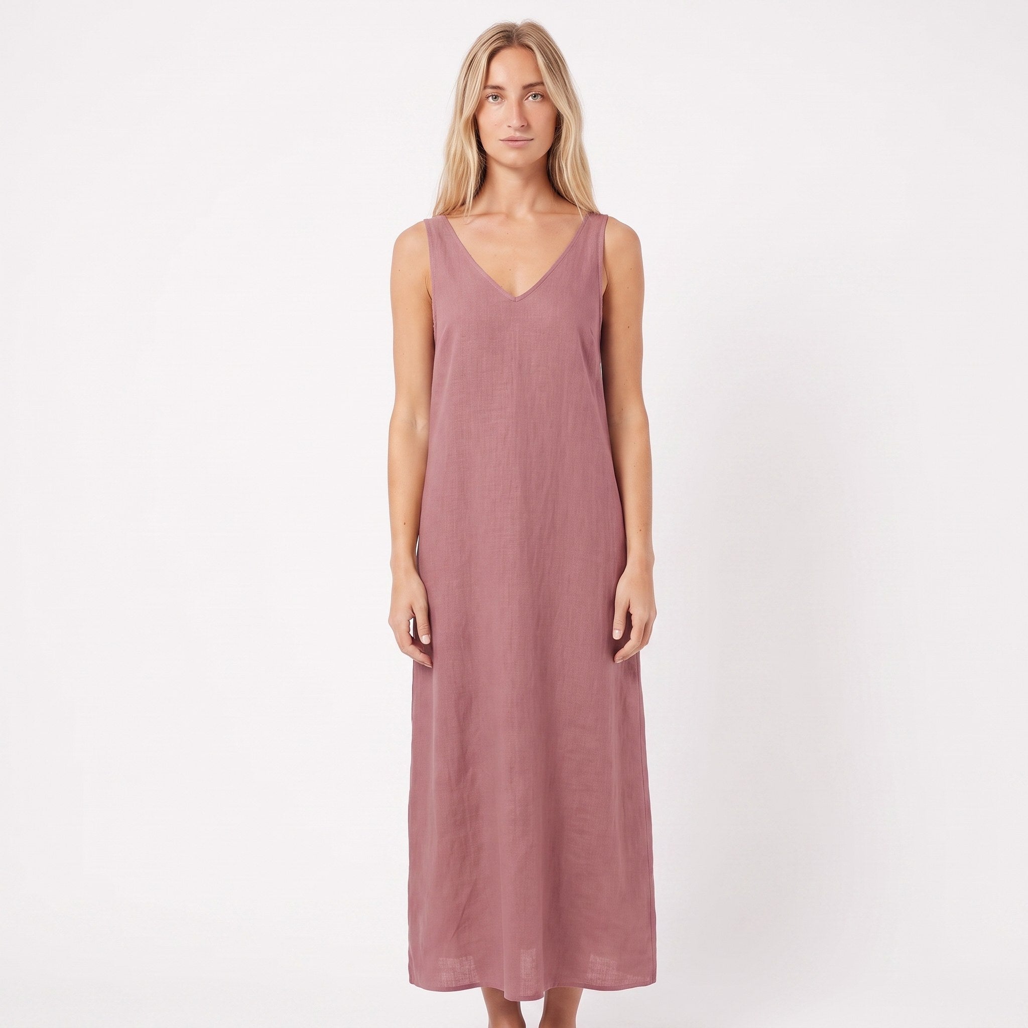 A woman modeling a sleeveless, V-neck maxi dress in a dusty rose pink color, standing against a plain white studio background.