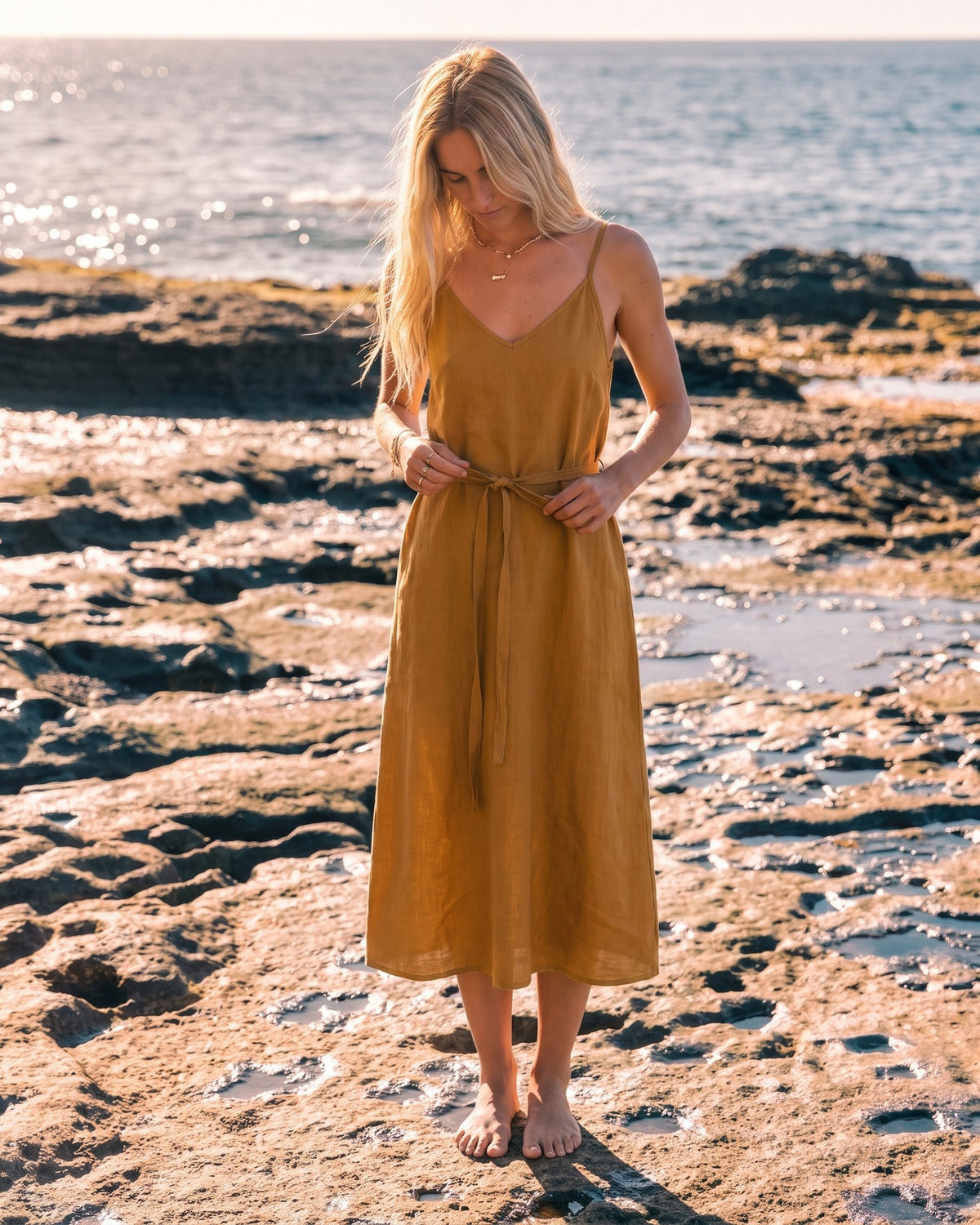 LeMuse SUNSET linen dress in ochre – model walking by the sea #Color_Ochre