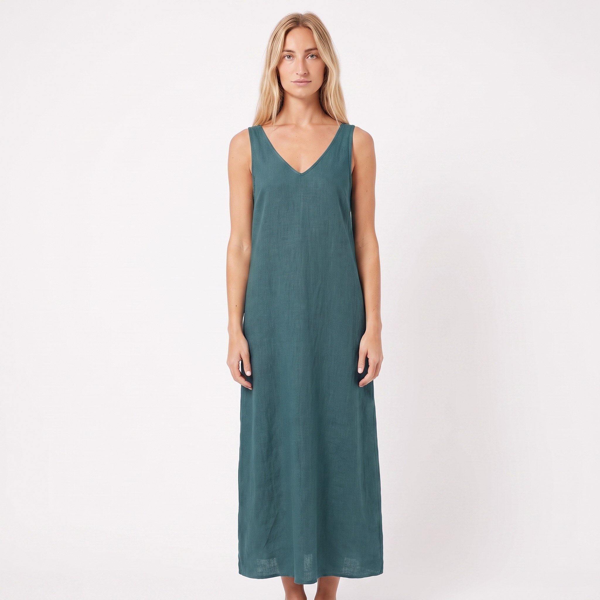A woman modeling a sleeveless, V-neck maxi dress in a muted teal green color, standing against a plain white studio background.